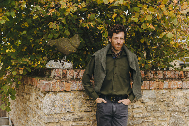 Green moleskin shirt on male model stood by brick wall