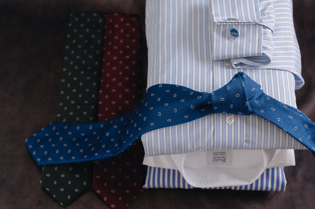 Stack of shirts with ties draped across on dark background