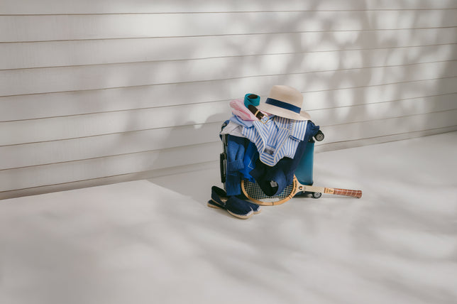 Summer Clothes draped on suitcase with tennis racket against white wooden boards