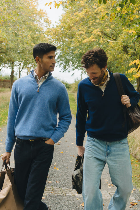 Two men wearing quarter zip jumpers walking with trees in background