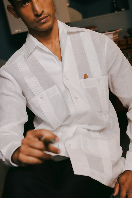 Man wearing a white button-up linen shirt with a blurred background and cigars in his pocket