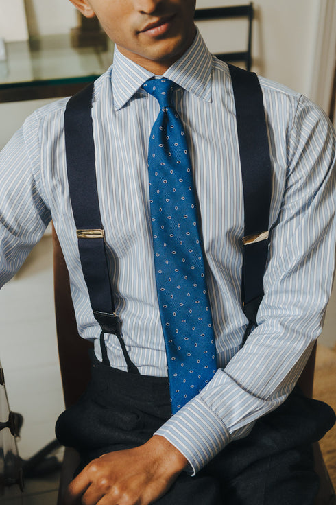 Person wearing a striped shirt, blue tie, and braces  indoors.