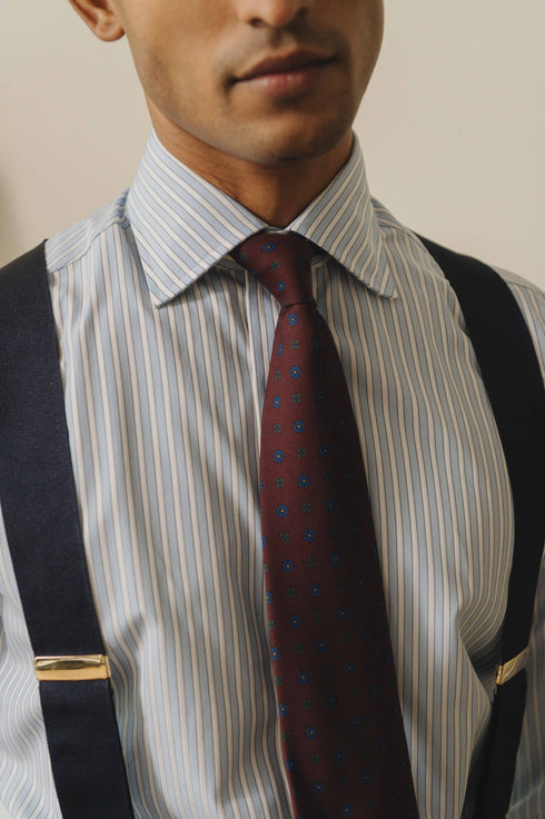 Man wearing a striped shirt, tie, and suspenders against a beige background