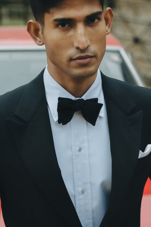 Man wearing a black tuxedo with a bow tie in front of a blurred background