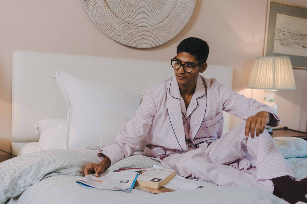 Person in a robe sitting on a bed with books and a lamp in the background
