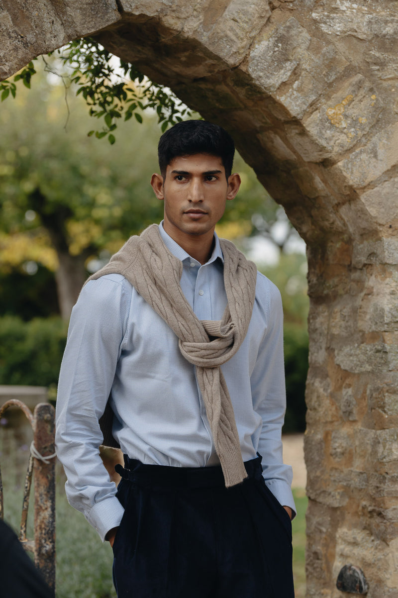 Male model stood in garden under brick arch wearing shirt and sweater over shoulders