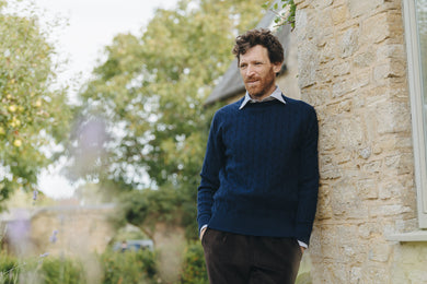 Man leaning against a stone wall outdoors with trees in the background