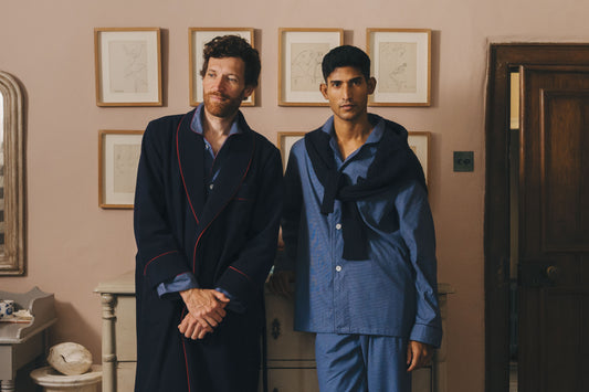Two men wearing matching blue pajama sets standing in a room with framed pictures on the wall.