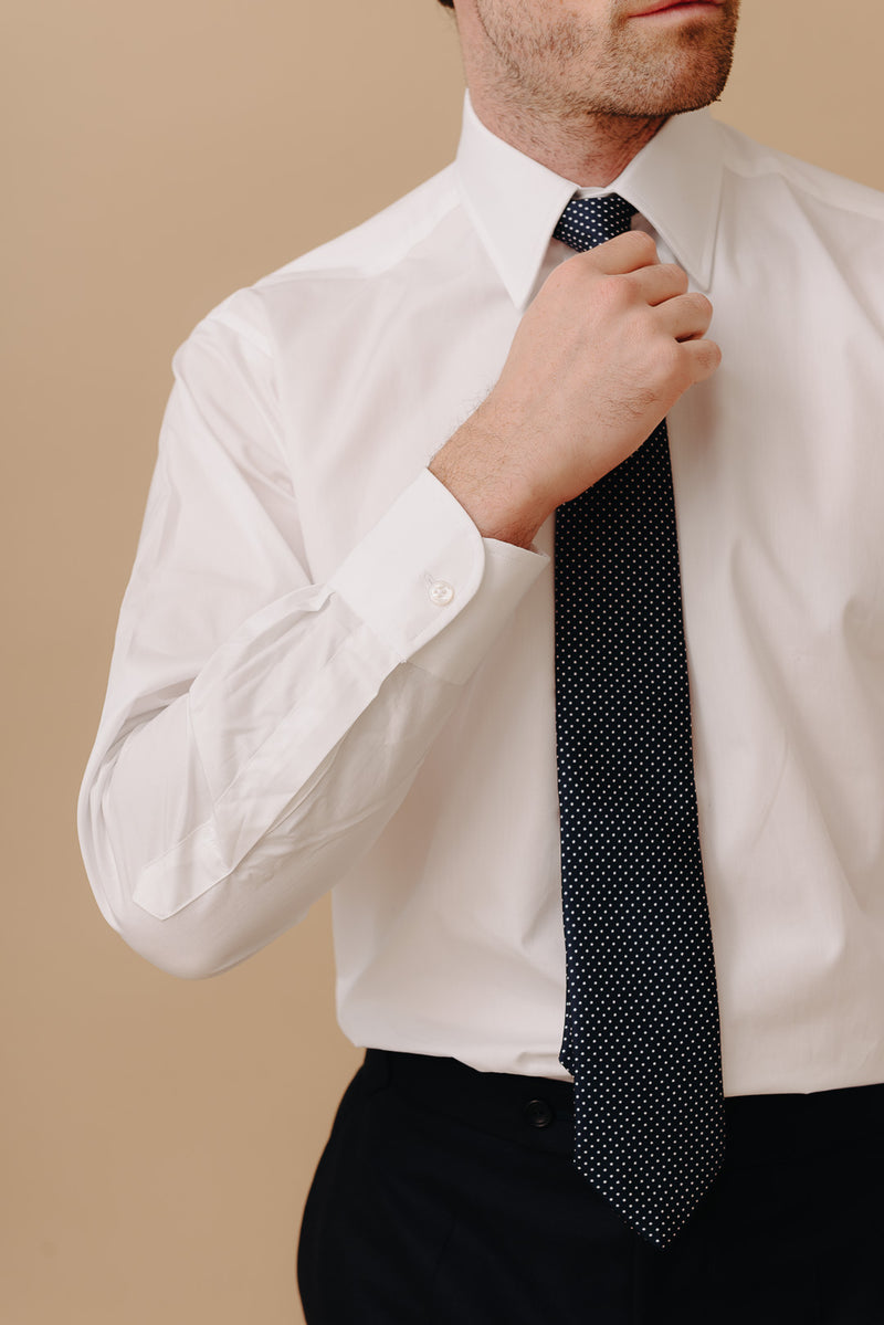 Man adjusting a black polka dot tie against a beige background