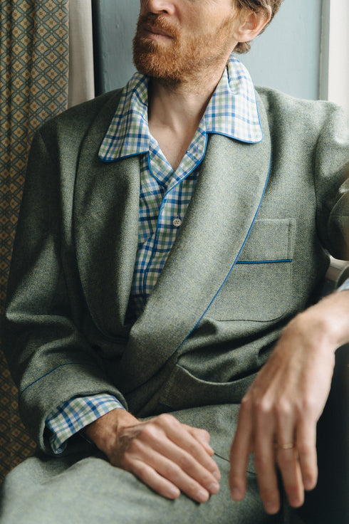 Man wearing a green dressing gown with a checkered nightshirt sitting indoors.