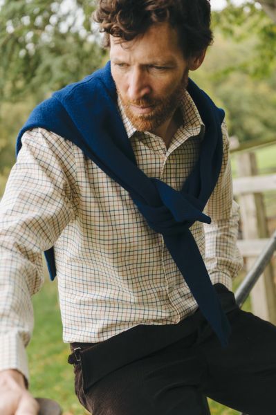 Man wearing a blue sweater over a checkered shirt outdoors