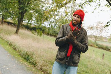 Person wearing a red beanie and gloves standing on a path with trees and grass in the background