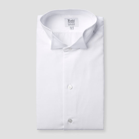 A folded white long-sleeve dress shirt with a spread collar and visible button placket, shown on a light gray background. The inner neck label reads Budd.