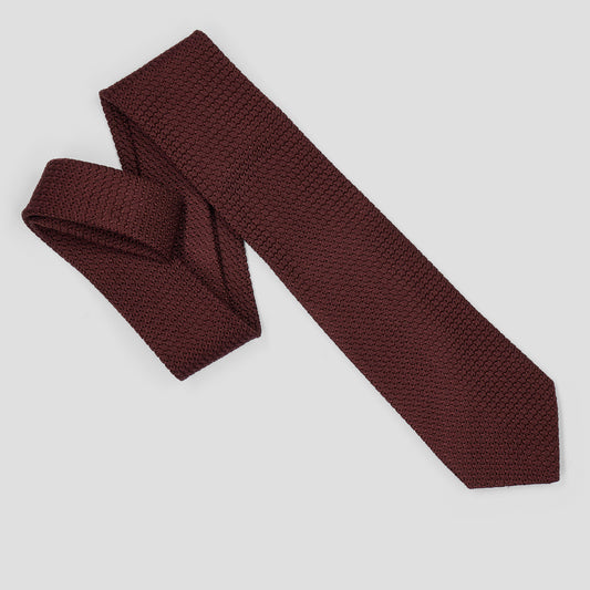 A textured burgundy necktie with a woven pattern, folded and laid out diagonally on a light gray background.