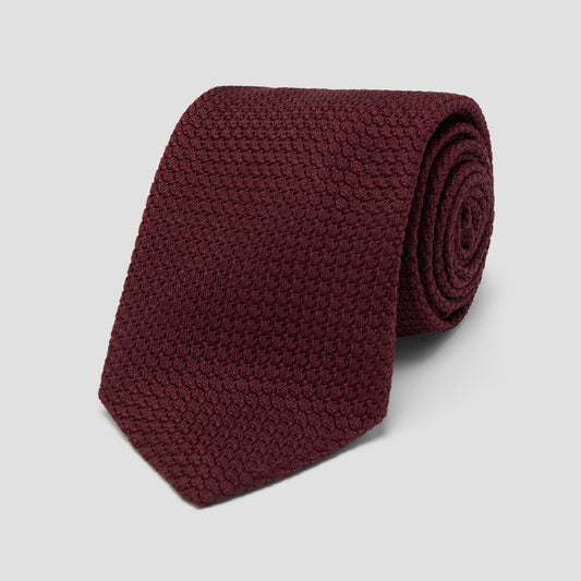 A rolled-up textured knit necktie in a deep burgundy color, displayed on a clean light gray background.
