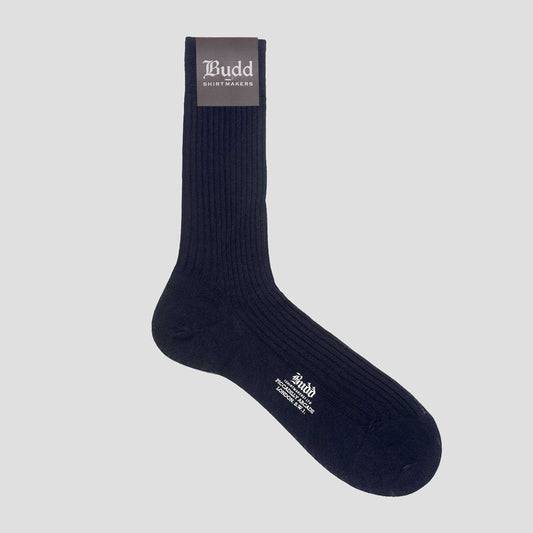 A single dark navy ribbed crew sock with white text branding on the toe and a dark brown cuff label reading 'Budd Shirtmakers', shown on a light gray background.