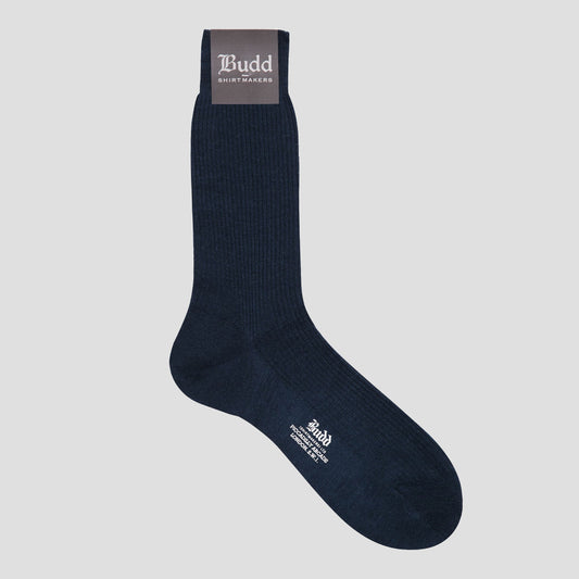 A single dark navy blue crew sock with white printed branding, shown against a solid light gray background. The sock features a dark gray cuff label with white text reading 'Budd Shirtmakers' and white text on the toe area.
