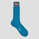 A single teal blue ribbed crew sock with a dark gray brand tag at the cuff and white 'The Budd Shirtmakers' logo printed on the toe, shown against a solid light gray background.