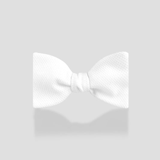 A white pre-tied bow tie with a subtle textured pattern, centered on a light gray background with a soft reflection underneath.