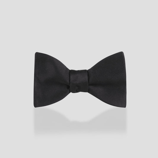 A classic black satin bow tie centered on a light gray background with a soft reflection underneath.