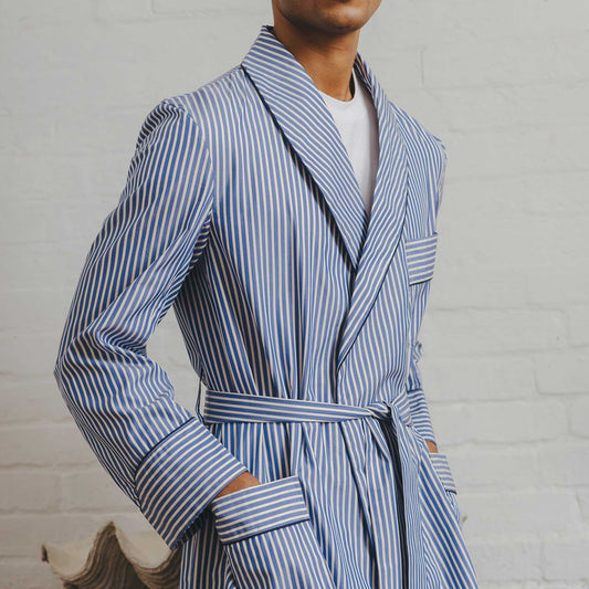 Male model wearing blue stripe dressing gown stood against white brick background
