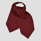 A burgundy silk necktie cravat with a small white micro-dot pattern, styled in a loose knot on a light gray background.