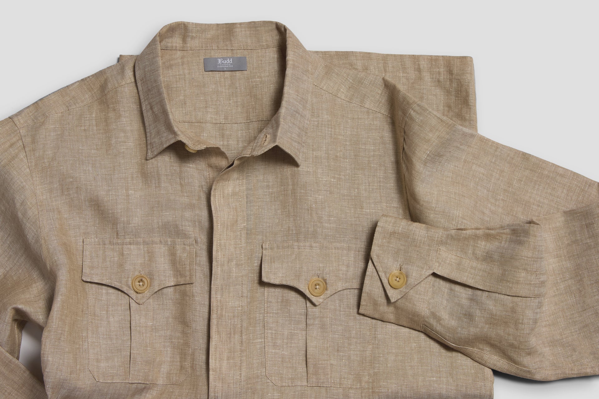 Sand beige coloured linen safari shirt laid with arm folded across front on white background