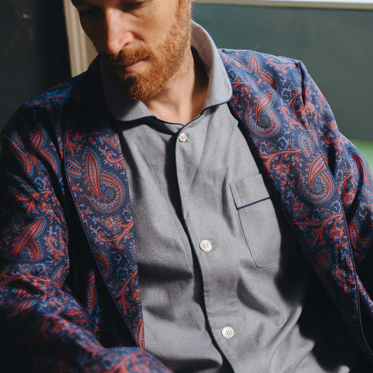 Man wearing a patterned dressing gown over a grey pyjama set with a blurred background