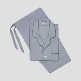A light blue-gray two-piece pajama set, featuring a folded long-sleeve button-up shirt with dark piping and a matching tie belt, laid flat on a light gray background.