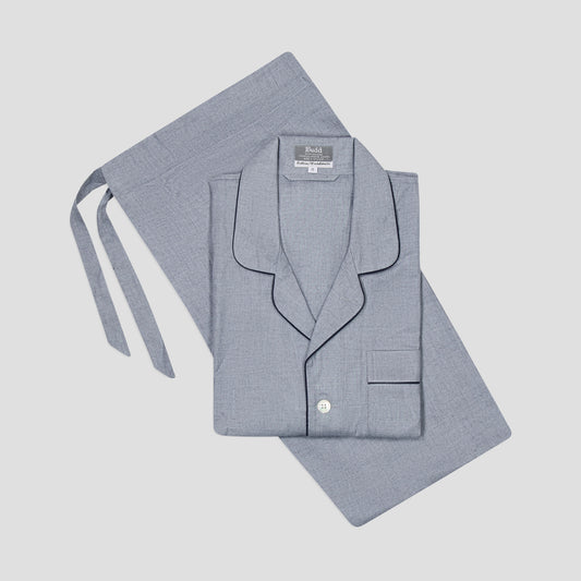 A light blue-gray two-piece pajama set, featuring a folded long-sleeve button-up shirt with dark piping and a matching tie belt, laid flat on a light gray background.