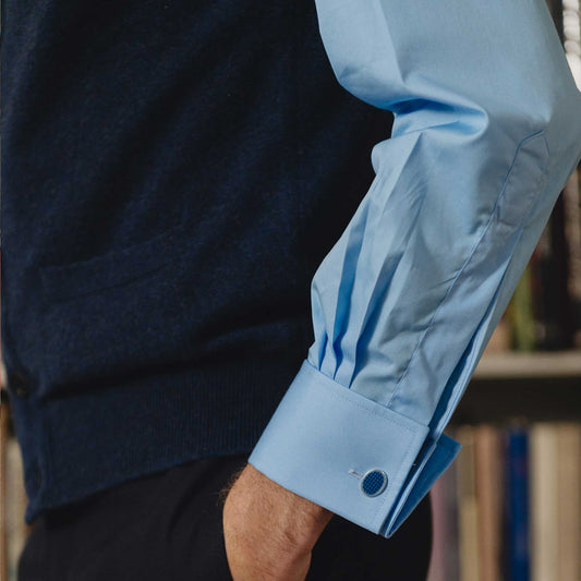 Close-up of a person wearing a navy sweater and light blue shirt with rolled-up sleeves.