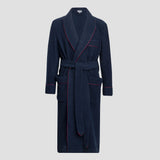 A navy blue terry cloth bathrobe with red piping trim, featuring a shawl collar, self-tie belt, and front patch pockets, shown against a light gray background.