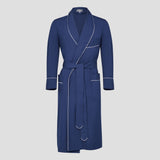 A navy blue long robe with white piping trim, featuring a shawl collar, self-tie belt, and front patch pockets, shown against a solid light gray background.
