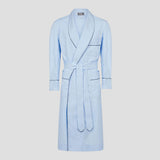 A light blue cotton bathrobe with dark piping trim, featuring a shawl collar, self-tie belt, and front patch pockets, shown against a neutral light gray background.