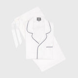 White pajama set with dark piping trim, including a long-sleeve button-front top with a tie neck and matching pants, laid flat on a light gray background.