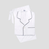 A folded white pajama set with black piping trim, including a long-sleeve button-front top with a collar and tie, and matching pants, shown on a light gray background.