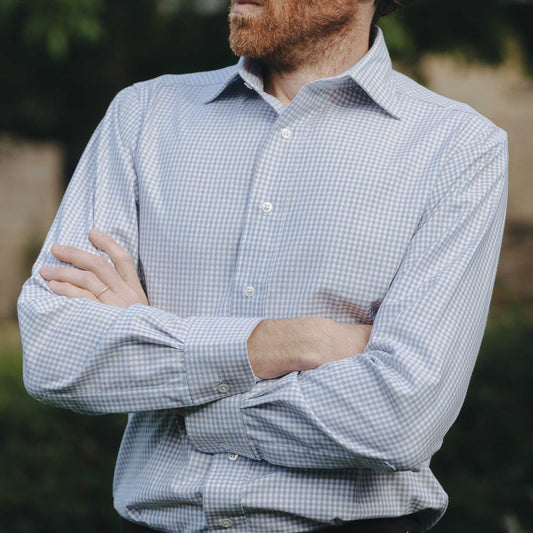 Man wearing a blue checkered shirt with arms crossed outdoors