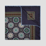 A square silk pocket square with a navy blue base, featuring a detailed geometric and floral medallion pattern in green, gold, and white, with a solid navy border and a folded corner showing the reverse pattern.