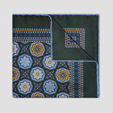 A square pocket square with a dark forest green base, featuring a detailed geometric and floral mandala pattern in blue, orange, and white. The pocket square is folded diagonally to show both the front patterned side and the solid dark green reverse side with its own border design, set against a plain light gray background.