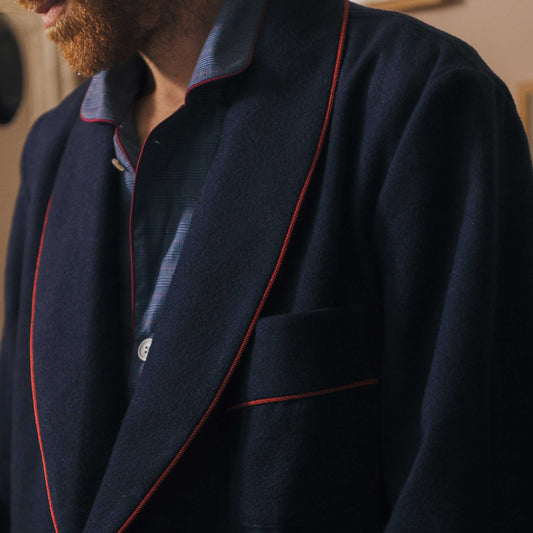Navy cashmere dressing gown with red piping worn by a person, blurred background
