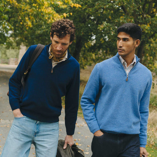 Two men wearing blue sweaters walking outdoors with trees in the background
