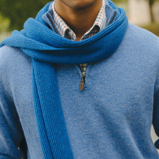 Close up neck detail of male model stood in field wearing blue quarter zip jumper with blue knitted scarf