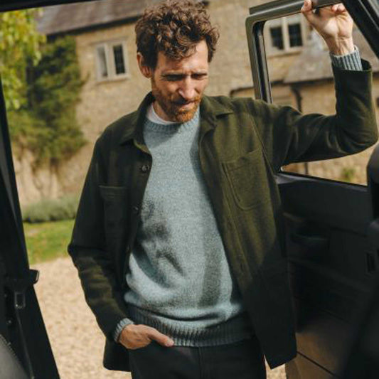 Man stood at car door in a rural setting wearing blue sweater