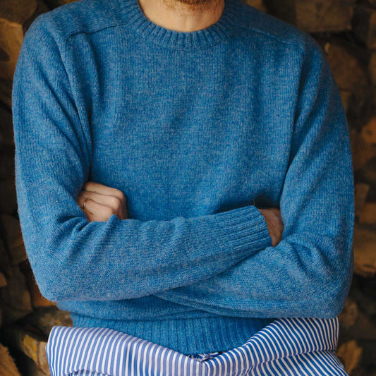 Person wearing a blue sweater with arms crossed, standing against a wooden background