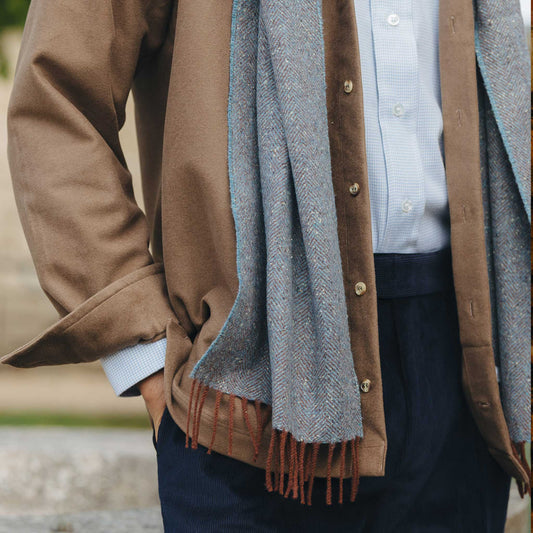 Person wearing a brown coat with a blue scarf and a blurred background