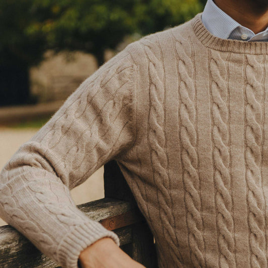 Close-up of a person wearing a beige cable knit sweater outdoors.