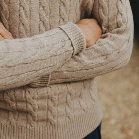 Close-up of a person wearing a beige cable knit sweater with blurred background