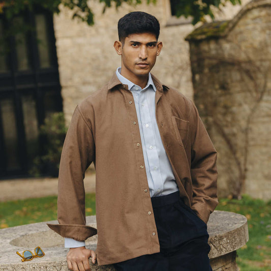 Man wearing a brown jacket over a light blue shirt outdoors.