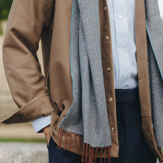 Person wearing a brown coat with a blue scarf and shirt, blurred background