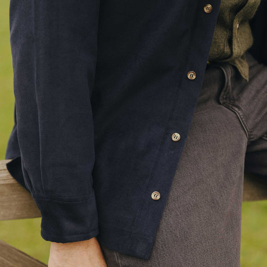 Person wearing a navy jacket with brown buttons on a blurred natural background